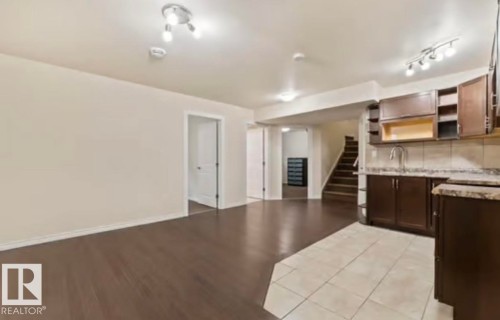 Open-concept living space featuring wood-finish flooring, recessed lighting, and a defined kitchen area with dark wood cabinetry, a sink, and stone-look countertops - 1944 67 Street, Edmonton, AB - Indoor Photo Showing Kitchen