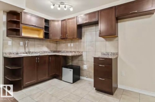 Kitchenette featuring dark wood-finish cabinetry, neutral tiled flooring, a granite-finish countertop, a stainless steel faucet, and track lighting - 1944 67 Street, Edmonton, AB - Indoor