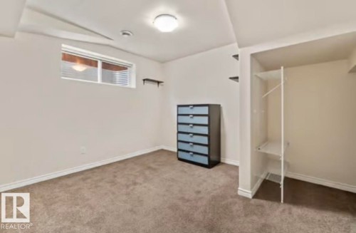Carpeted interior space featuring a built-in closet with shelving and hanging rod, a window with horizontal blinds, and a flush mount ceiling light - 1944 67 Street, Edmonton, AB - Indoor