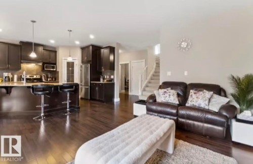 Open-concept living area featuring rich wood-finish flooring, a contemporary kitchen with dark cabinetry, stainless steel appliances, and a central island with pendant lighting - 1944 67 Street, Edmonton, AB - Indoor