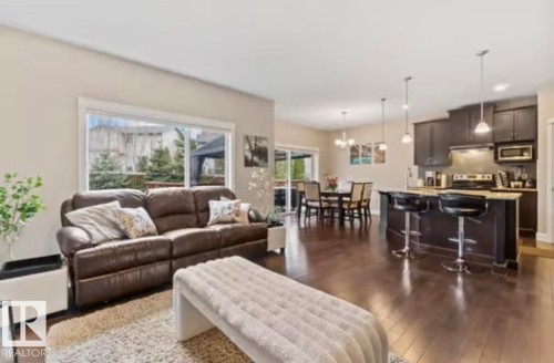 Open-concept living space featuring wood-finish flooring, a kitchen island with pendant lighting, dark cabinetry, and a dining area with a sliding glass door - 1944 67 Street, Edmonton, AB - Indoor Photo Showing Living Room