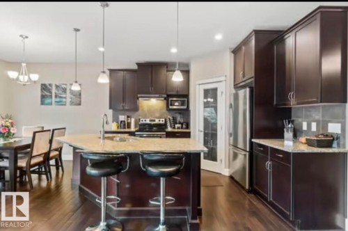 Open-concept kitchen featuring an island with a breakfast bar, dark wood-finish cabinetry, light-toned countertops, and wood-finish flooring - 1944 67 Street, Edmonton, AB - Indoor Photo Showing Kitchen With Stainless Steel Kitchen With Upgraded Kitchen