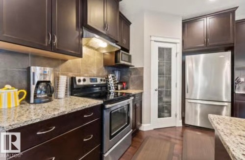 Kitchen featuring dark wood cabinetry, light speckled countertops, stainless steel appliances, and wood-finish flooring - 1944 67 Street, Edmonton, AB - Indoor Photo Showing Kitchen With Stainless Steel Kitchen With Upgraded Kitchen