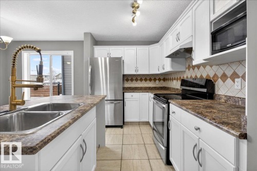 Kitchen with stainless steel appliances, white cabinets, a textured ceiling, under cabinet range hood, and dark countertops - 150 Acacia Circle, Leduc, AB - Indoor Photo Showing Kitchen With Double Sink