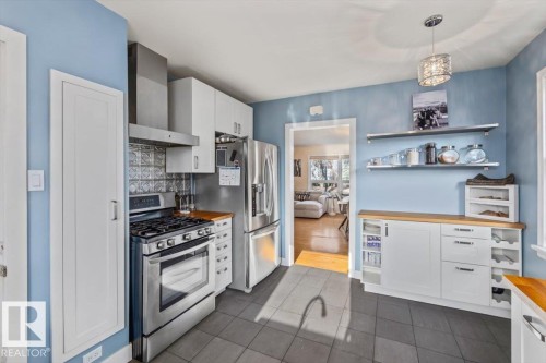 Kitchen featuring stainless steel appliances, white cabinetry, wood-finish countertops, and tile flooring - 10756 133 Street, Edmonton, AB - Indoor Photo Showing Kitchen