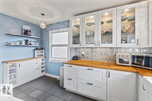 Kitchen featuring white cabinetry with glass-front upper cabinets, wood-finish countertops, and a decorative tile backsplash - 10756 133 Street, Edmonton, AB - Indoor Photo Showing Kitchen
