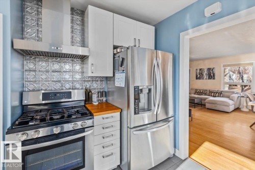 Contemporary kitchen featuring stainless steel appliances, a gas range with an overhead vent hood, white cabinetry, a wood-finish countertop, and a decorative tile backsplash - 10756 133 Street, Edmonton, AB - Indoor Photo Showing Kitchen