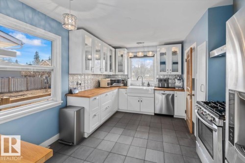 Kitchen featuring white shaker cabinetry, wood-finish countertops, stainless steel appliances, and a farmhouse-style sink - 10756 133 Street, Edmonton, AB - Indoor Photo Showing Kitchen