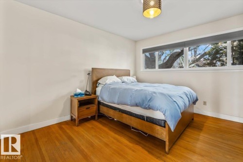 Bright room featuring a multi-pane window with roller shades, wood-finish flooring, and a decorative ceiling light fixture - 10756 133 Street, Edmonton, AB - Indoor Photo Showing Bedroom