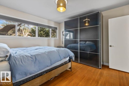 Hardwood flooring complementing a modern built-in wardrobe with smoked glass doors - 10756 133 Street, Edmonton, AB - Indoor Photo Showing Bedroom