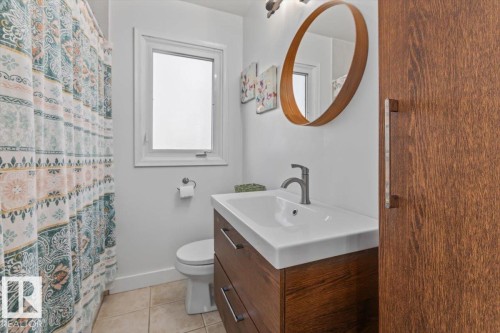 Bathroom featuring a modern wood-finish vanity with an integrated sink, a single-handle faucet, and a circular framed mirror - 10756 133 Street, Edmonton, AB - Indoor Photo Showing Bathroom