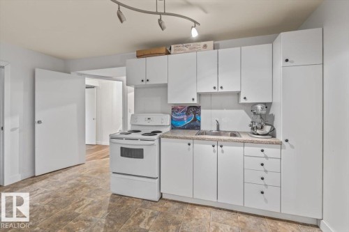 Kitchen area featuring white cabinetry with black hardware, a stainless steel sink, and a white electric range - 10756 133 Street, Edmonton, AB - Indoor Photo Showing Kitchen