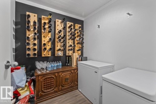 Dedicated storage area featuring multiple wall-mounted wine racks, a decorative wooden console table, durable wood-finish flooring, and crisp white walls - 10756 133 Street, Edmonton, AB - Indoor Photo Showing Laundry Room