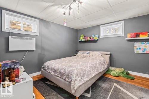 Room featuring wood-finish flooring, a neutral wall color, two windows with blinds, a wall-mounted heating unit, and an overhead track lighting fixture - 10756 133 Street, Edmonton, AB - Indoor Photo Showing Bedroom