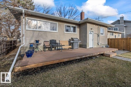 Rear exterior featuring a spacious wooden deck with a single step, stucco siding, multiple windows with white trim, and a private wooden fence - 10756 133 Street, Edmonton, AB - Outdoor With Deck Patio Veranda