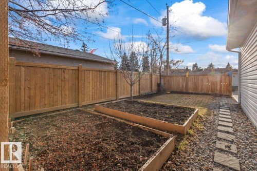 Fenced backyard featuring two raised garden beds, a gravel pathway with stepping stones, and a side exterior clad in horizontal siding - 10756 133 Street, Edmonton, AB - Outdoor