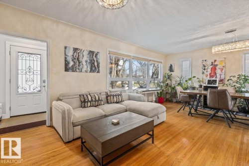 Living area featuring wood-finish flooring, a decorative front entry door with a wrought iron insert, and large windows - 10756 133 Street, Edmonton, AB - Indoor Photo Showing Living Room