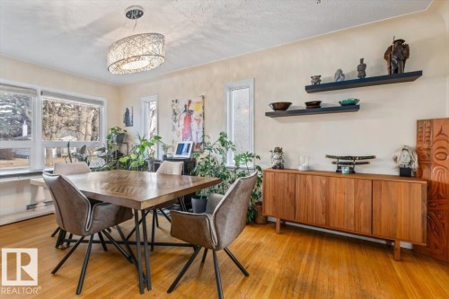 Dining area featuring wood-finish flooring, a contemporary chandelier, multiple windows, and a built-in wood-tone credenza with floating shelves - 10756 133 Street, Edmonton, AB - Indoor Photo Showing Dining Room