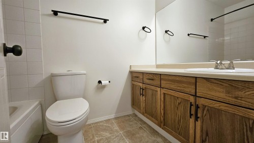 Bathroom featuring a wood-finish vanity with a light-colored countertop, an integrated sink with a chrome faucet, and a large wall-mounted mirror - 415 15503 106 Street, Edmonton, AB - Indoor Photo Showing Bathroom