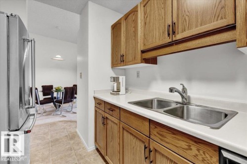 Kitchen featuring wood cabinetry, a stainless steel double-basin sink with a chrome faucet, and white countertops - 415 15503 106 Street, Edmonton, AB - Indoor Photo Showing Kitchen With Double Sink