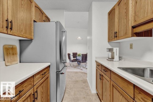 Kitchen featuring wood-finish cabinetry, white countertops, a stainless steel refrigerator, and a stainless steel sink - 415 15503 106 Street, Edmonton, AB - Indoor Photo Showing Kitchen