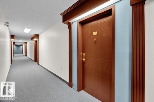 Entry door with gold-tone hardware, a door knocker, and a number plate, framed by decorative wood molding - 415 15503 106 Street, Edmonton, AB - Indoor Photo Showing Other Room