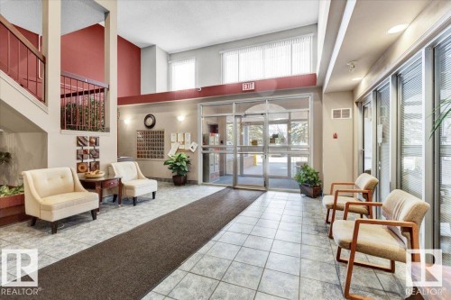 Spacious lobby featuring tile flooring, a two-story ceiling, abundant natural light, glass entry doors, and a staircase with a dark wood railing - 415 15503 106 Street, Edmonton, AB - Indoor Photo Showing Other Room