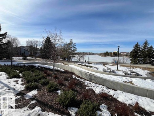 Landscaped grounds featuring a concrete retaining wall, mature evergreen trees, and a distant lake - 415 15503 106 Street, Edmonton, AB - Outdoor With View