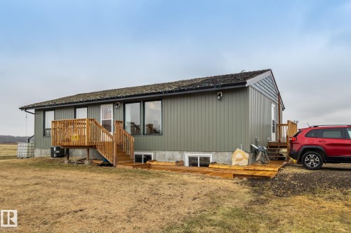 Ranch-style residence featuring horizontal siding, a natural wood deck with stairs, multiple large windows, and a shingled roof - 23127 Twp Rd 502, Rural Leduc County, AB - Outdoor