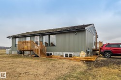 Ranch-style residence featuring horizontal siding, a natural wood deck with stairs, multiple large windows, and a shingled roof - 