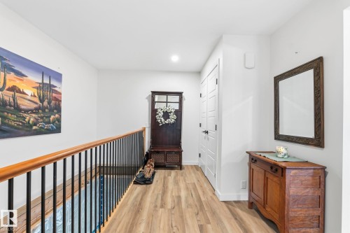 Light wood-finish flooring extending throughout a hallway featuring white walls, a staircase with a wood handrail and black metal balusters, and white paneled doors - 23127 Twp Rd 502, Rural Leduc County, AB - Indoor Photo Showing Other Room