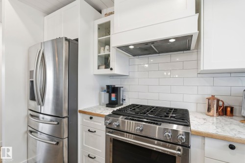 Modern kitchen featuring white shaker cabinetry, stainless steel appliances, a gas range with a matching range hood, a white subway tile backsplash, and a combination of wood and stone-finish countertops - 23127 Twp Rd 502, Rural Leduc County, AB - Indoor Photo Showing Kitchen With Upgraded Kitchen