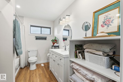 Bathroom featuring wood-finish flooring, a white vanity with an integrated sink, an oval mirror, and an adjacent built-in shelving unit - 23127 Twp Rd 502, Rural Leduc County, AB - Indoor Photo Showing Bathroom