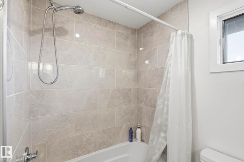 Bathtub with neutral-toned rectangular wall tiling, a chrome shower fixture, and a white window frame - 23127 Twp Rd 502, Rural Leduc County, AB - Indoor Photo Showing Bathroom
