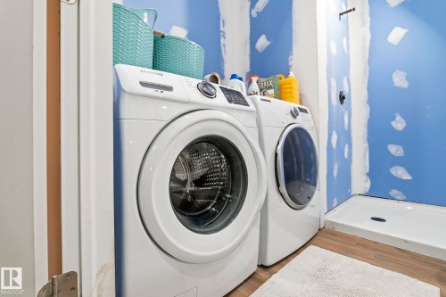 Laundry area featuring a front-loading washer and dryer, wood-finish flooring, and a shower pan with a dark drain - 23127 Twp Rd 502, Rural Leduc County, AB - Indoor Photo Showing Laundry Room