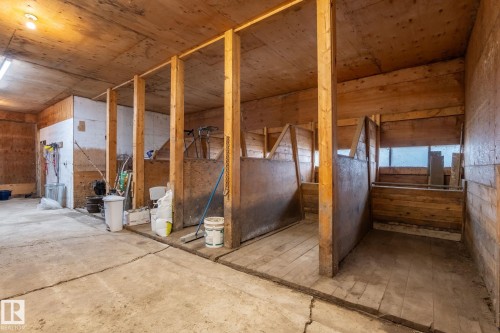 Interior barn space featuring multiple stalls with wood construction, concrete flooring, and an exposed wood ceiling - 23127 Twp Rd 502, Rural Leduc County, AB - Indoor