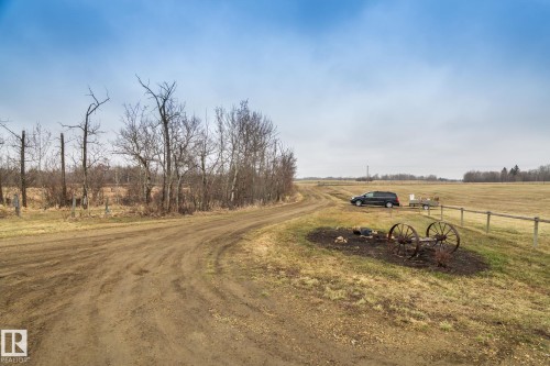 Rural property featuring an unpaved road, mature trees, open fields, and a rustic wagon wheel decorative element - 23127 Twp Rd 502, Rural Leduc County, AB - Outdoor With View