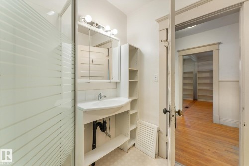 Bathroom featuring a frosted glass shower enclosure, a white pedestal sink with an integrated countertop, a mirrored medicine cabinet with overhead vanity lighting, and open shelving storage - 10921 126 Street, Edmonton, AB - Indoor Photo Showing Bathroom