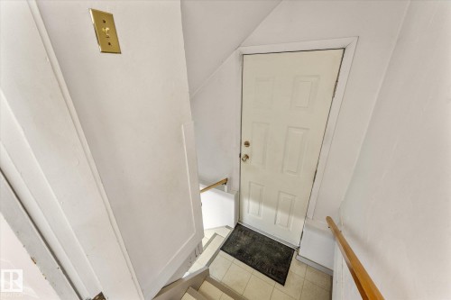 Stairwell featuring white paneling, a wooden handrail, and a four-panel door with brass hardware - 10921 126 Street, Edmonton, AB - Indoor Photo Showing Other Room