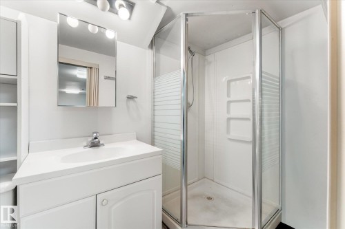 Bathroom featuring a corner shower with glass enclosure, white vanity with integrated sink, chrome faucet, wall-mounted mirror, and overhead vanity lighting - 10921 126 Street, Edmonton, AB - Indoor Photo Showing Bathroom