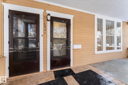 Inviting front porch featuring a light beige siding, two dark-paneled screen doors, and decorative arched windows - 10921 126 Street, Edmonton, AB - Outdoor With Exterior