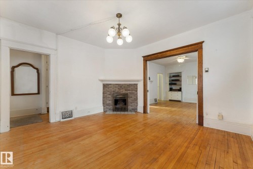 Hardwood flooring throughout featuring a brick fireplace with a white mantel, traditional chandelier, and a wide cased opening with wood trim - 10921 126 Street, Edmonton, AB - Indoor With Fireplace