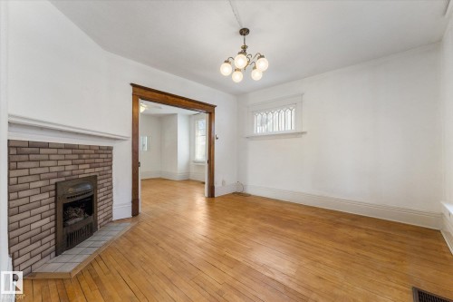 Spacious room featuring wood-finish flooring, a brick fireplace with a tile hearth, a decorative chandelier, and an ornate transom window - 10921 126 Street, Edmonton, AB - Indoor With Fireplace