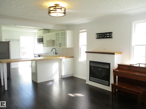 Modern kitchen and living area featuring dark wood-finish flooring - 12115 64 Street Nw, Edmonton, AB - Indoor Photo Showing Other Room With Fireplace