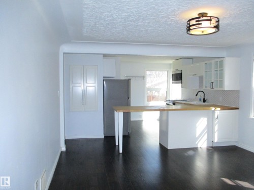 Open-concept kitchen with dark wood-finish flooring, white cabinetry, integrated stainless steel appliances, and a light-toned countertop with an extended breakfast bar - 12115 64 Street Nw, Edmonton, AB - Indoor Photo Showing Kitchen