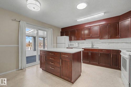 Kitchen featuring rich wood cabinetry, a central island with a solid surface countertop, white subway tile backsplash, and a sliding glass door opening to an outdoor patio - 1542 54 Street, Edmonton, AB - Indoor Photo Showing Kitchen