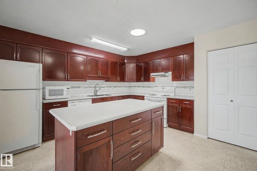 Kitchen featuring dark wood-finish cabinetry with silver hardware, white subway tile backsplash, and a central island with a light-toned countertop - 1542 54 Street, Edmonton, AB - Indoor Photo Showing Kitchen