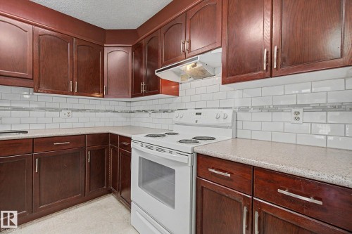Kitchen featuring dark wood cabinetry, white subway tile backsplash with decorative accent, light speckled countertops, and a white electric range - 1542 54 Street, Edmonton, AB - Indoor Photo Showing Kitchen