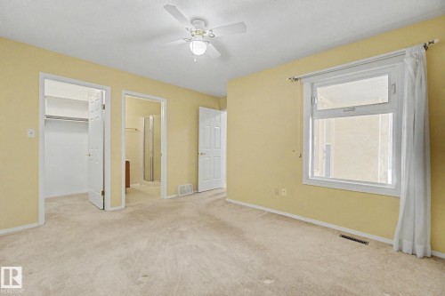 Carpeted room featuring a ceiling fan with integrated lighting, a window with white trim and curtains, and direct access to a closet and a bathroom with a glass-enclosed shower - 1542 54 Street, Edmonton, AB - Indoor Photo Showing Other Room