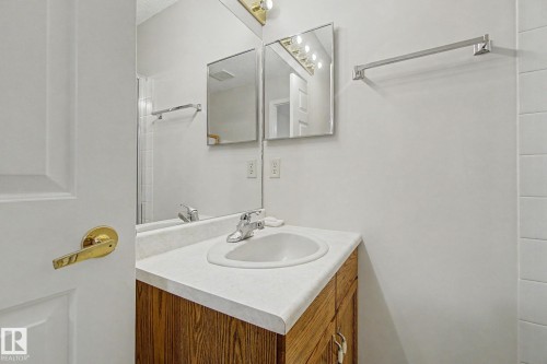 Bathroom vanity featuring a wood-finish cabinet, white countertop, and an integrated sink with a chrome faucet - 1542 54 Street, Edmonton, AB - Indoor Photo Showing Bathroom